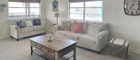 A living room with two sofas, a coffee table, a clock on the wall, and a ceiling fan.