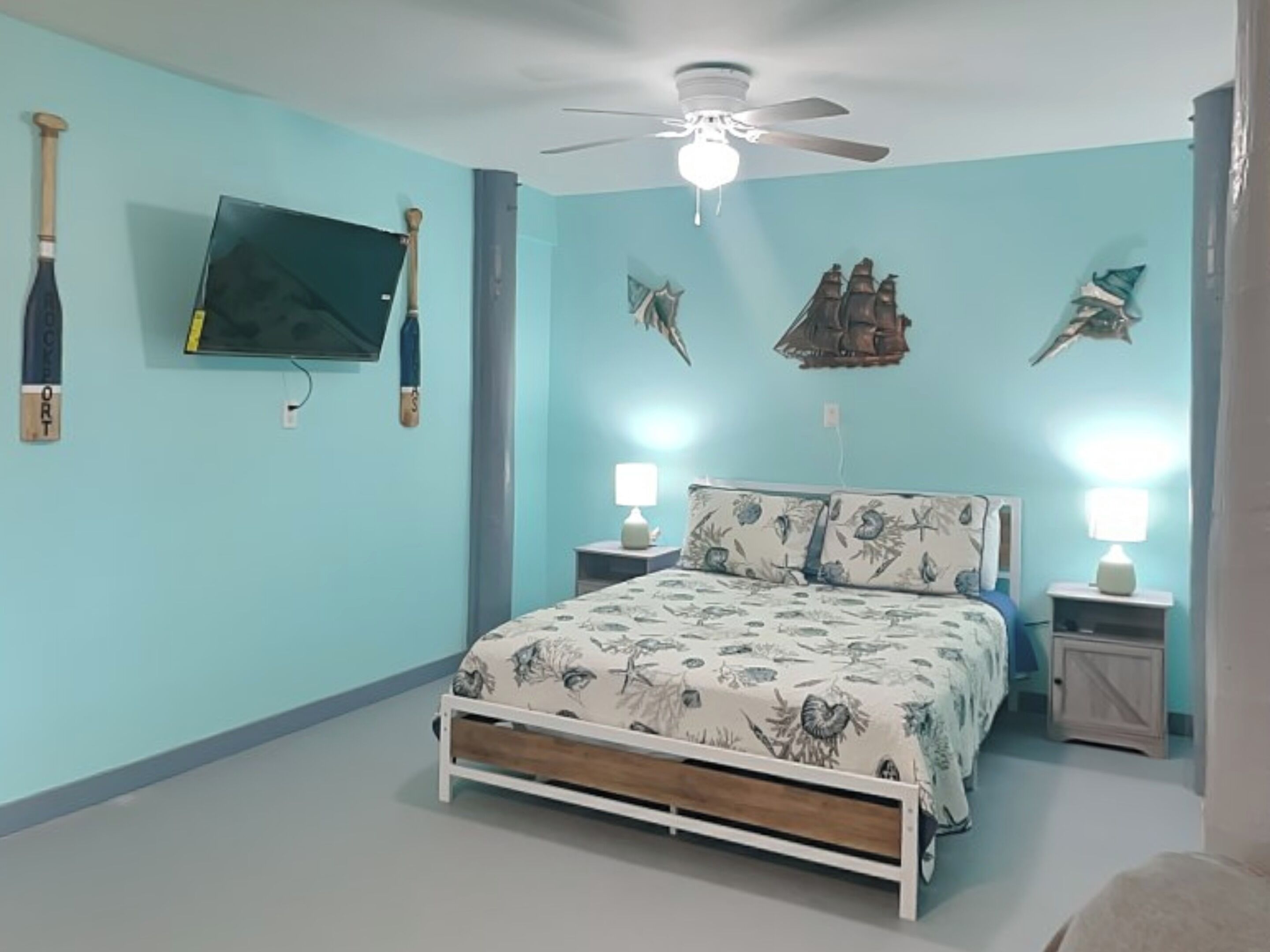 A bedroom with a bed, two bedside tables, a ceiling fan, wall-mounted TV, and decorative wall art.