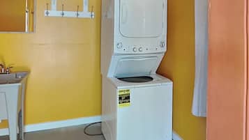 A compact laundry room with a front-loading washer and dryer, a small sink, and a mirror above the sink.