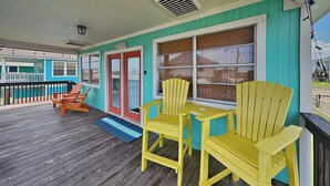 Una terraza de madera con sillas Adirondack amarillas y una puerta roja.