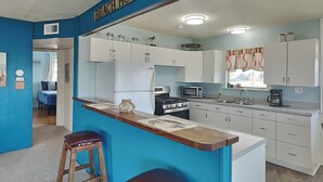 Een keuken met een blauwe accentmuur, witte kasten, een fornuis, een magnetron en twee krukken.