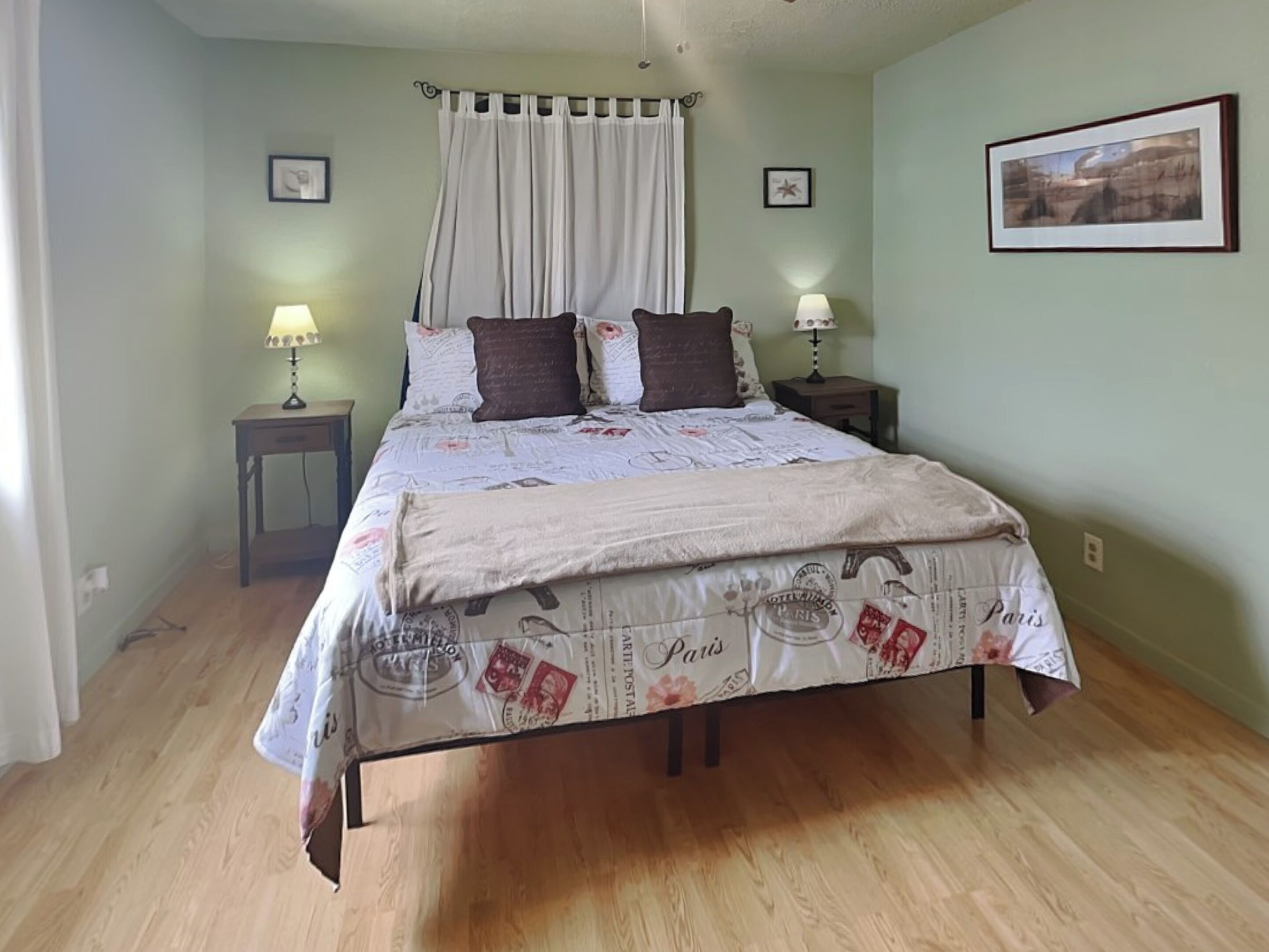 Een slaapkamer met een bed, twee nachtkastjes, een raam met gordijnen en een ingelijst schilderij aan de muur.