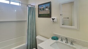 Een badkamer met een bad, toilet, wastafel en een ingelijste foto aan de muur.