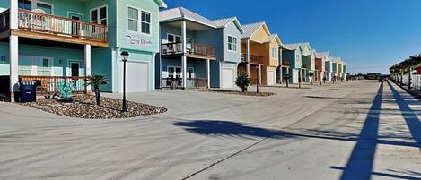 A row of colorful beachfront buildings with balconies, a clear sky, and a wide road.