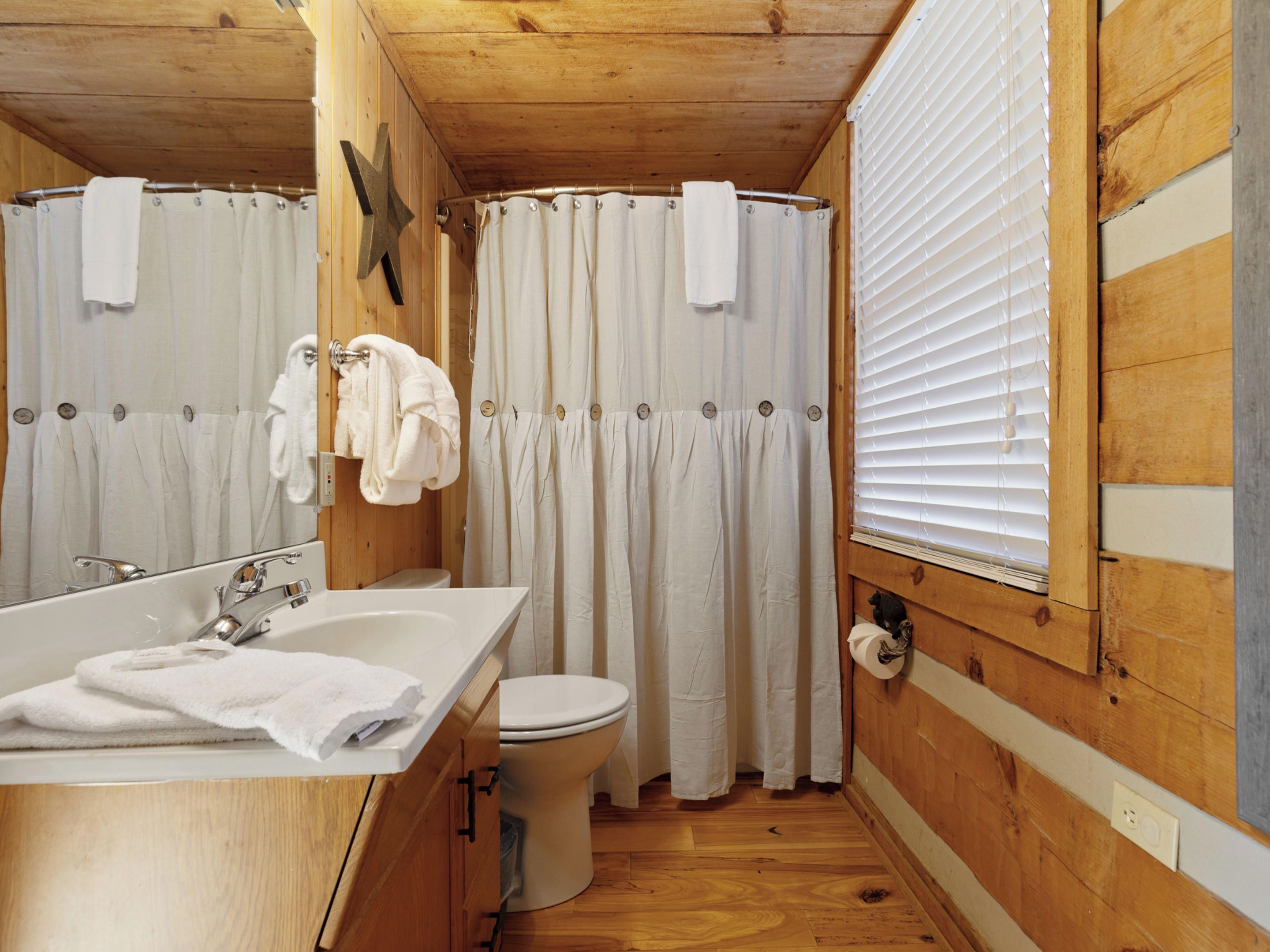 Un baño de madera con lavamanos, inodoro y cortina de ducha.