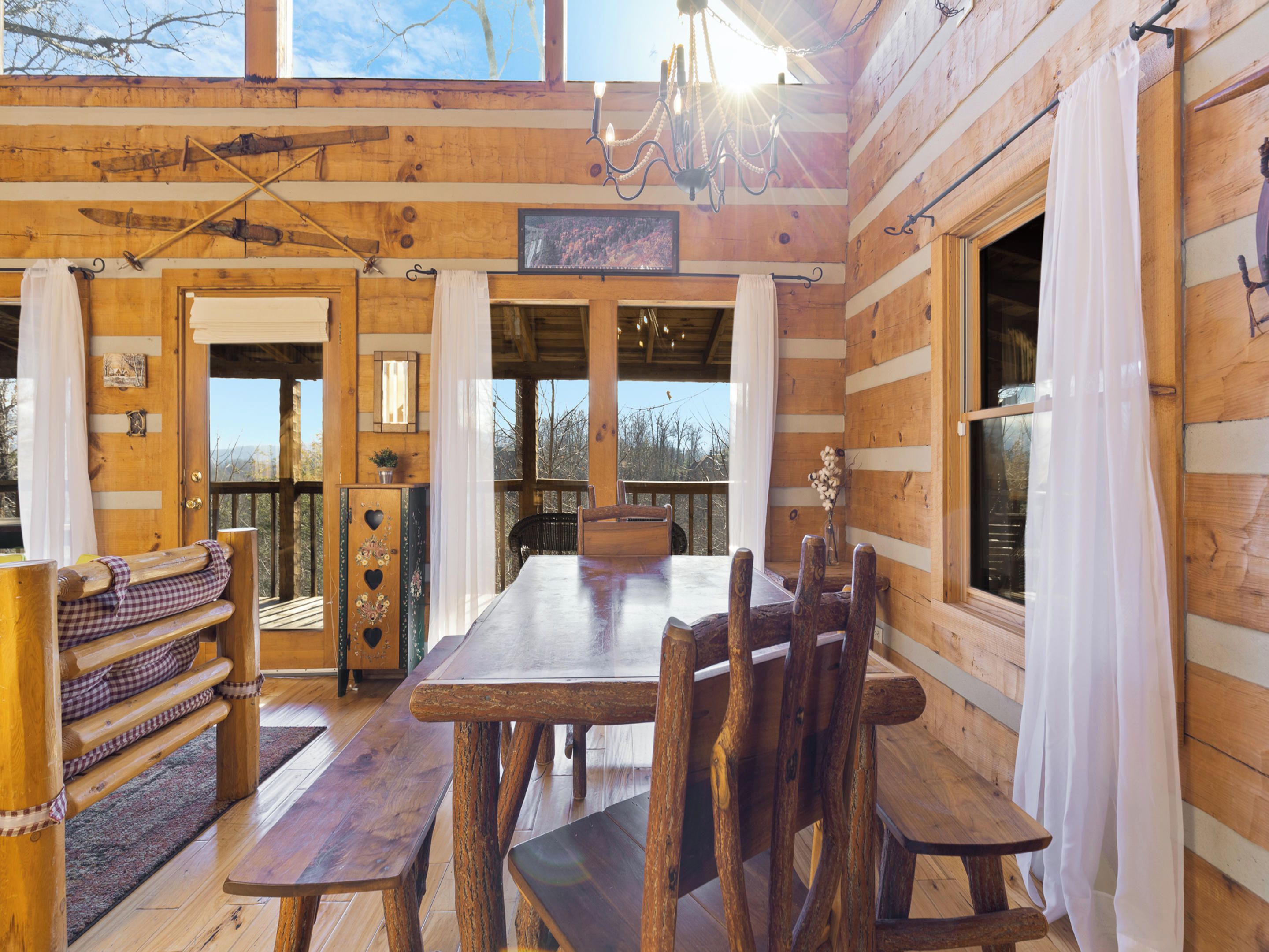 A rustic wooden cabin interior with a large dining table, benches, and a chandelier.