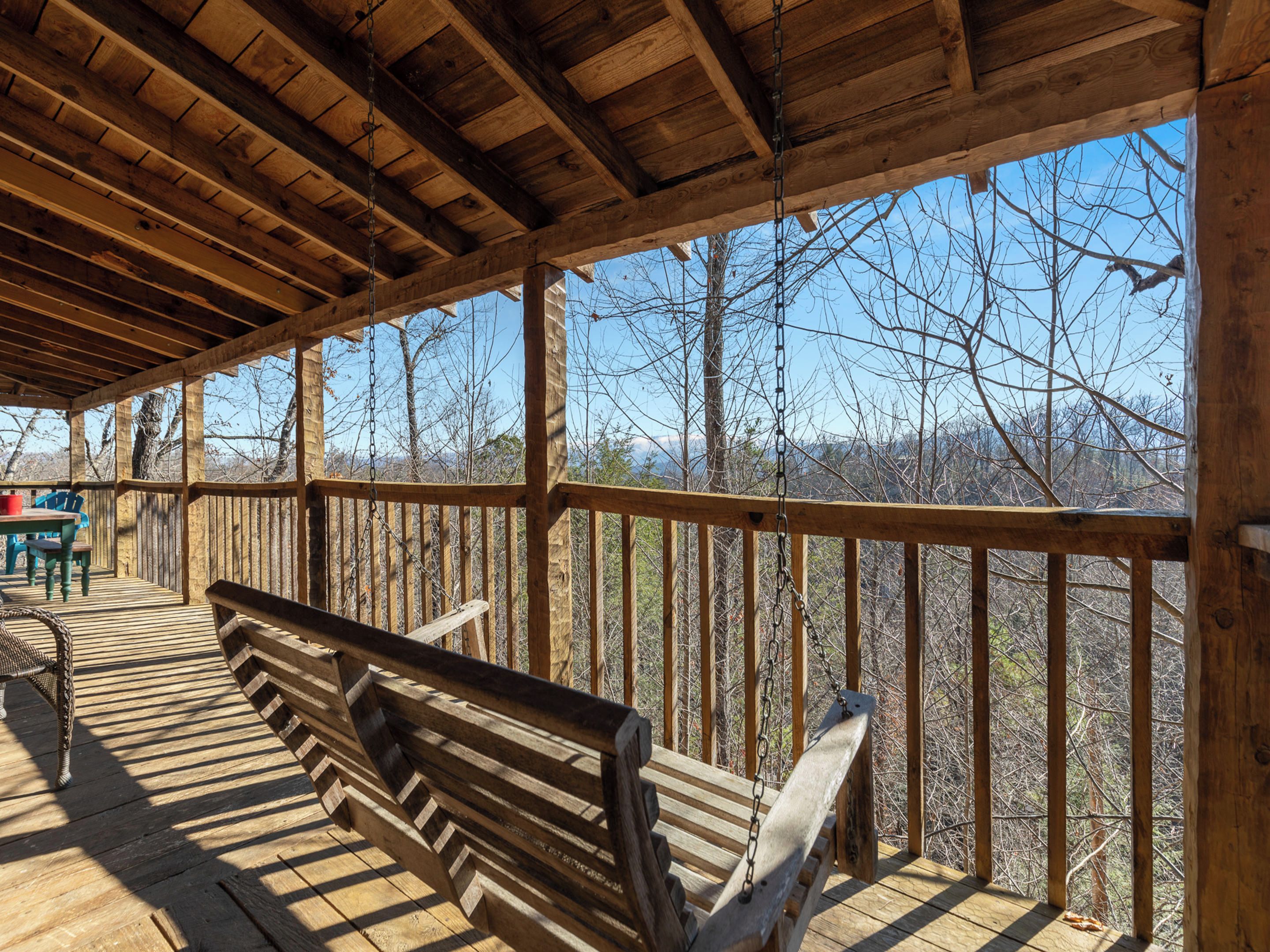 A covered wooden deck with a bench, overlooking a forested area.