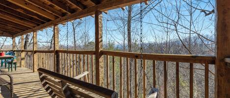 A covered wooden deck with a bench, overlooking a forested area.