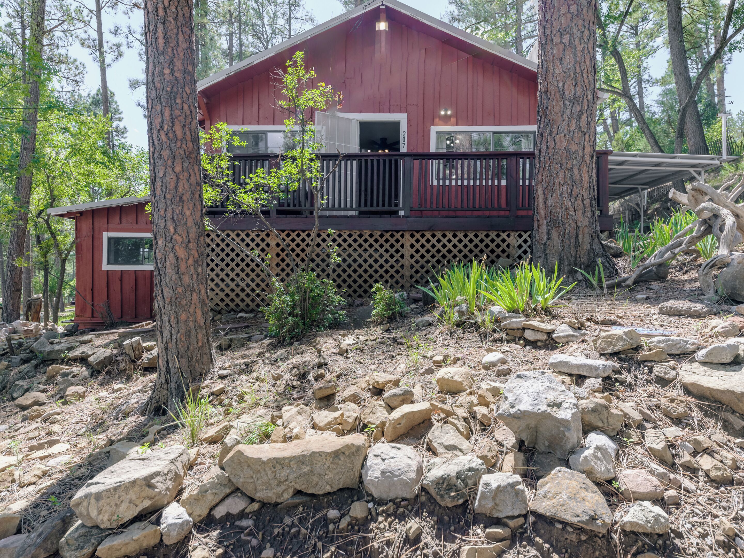 A red cabin with a deck, surrounded by trees and rocks.