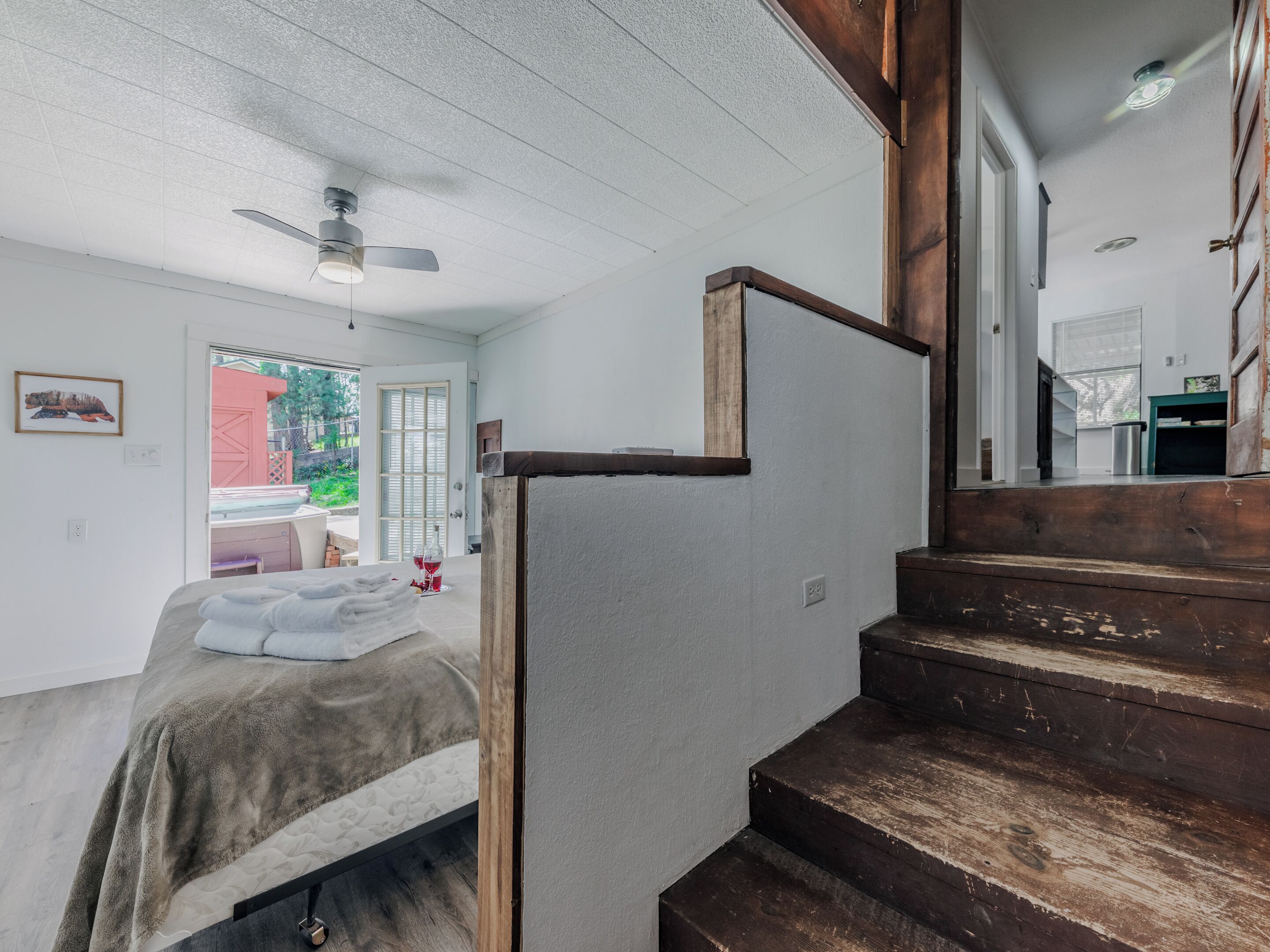 A bedroom with a bed, a wooden staircase, and a door leading to another room.