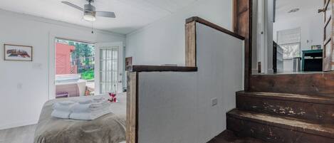 A bedroom with a bed, a wooden staircase, and a door leading to another room.