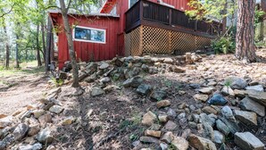 Una baita di legno rossa con un balcone, circondata da alberi e da un terreno roccioso.