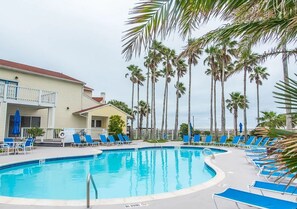 A pool area with lounge chairs and palm trees. - Toes In The Water II by Silver Sands Vacation Rentals (Port Aransas)