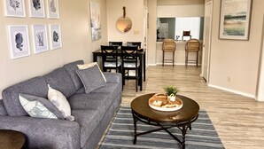 A living room with a gray sofa, a round coffee table with a tray, and framed artwork on the walls. - Toes In The Water II by Silver Sands Vacation Rentals (Corpus Christi)