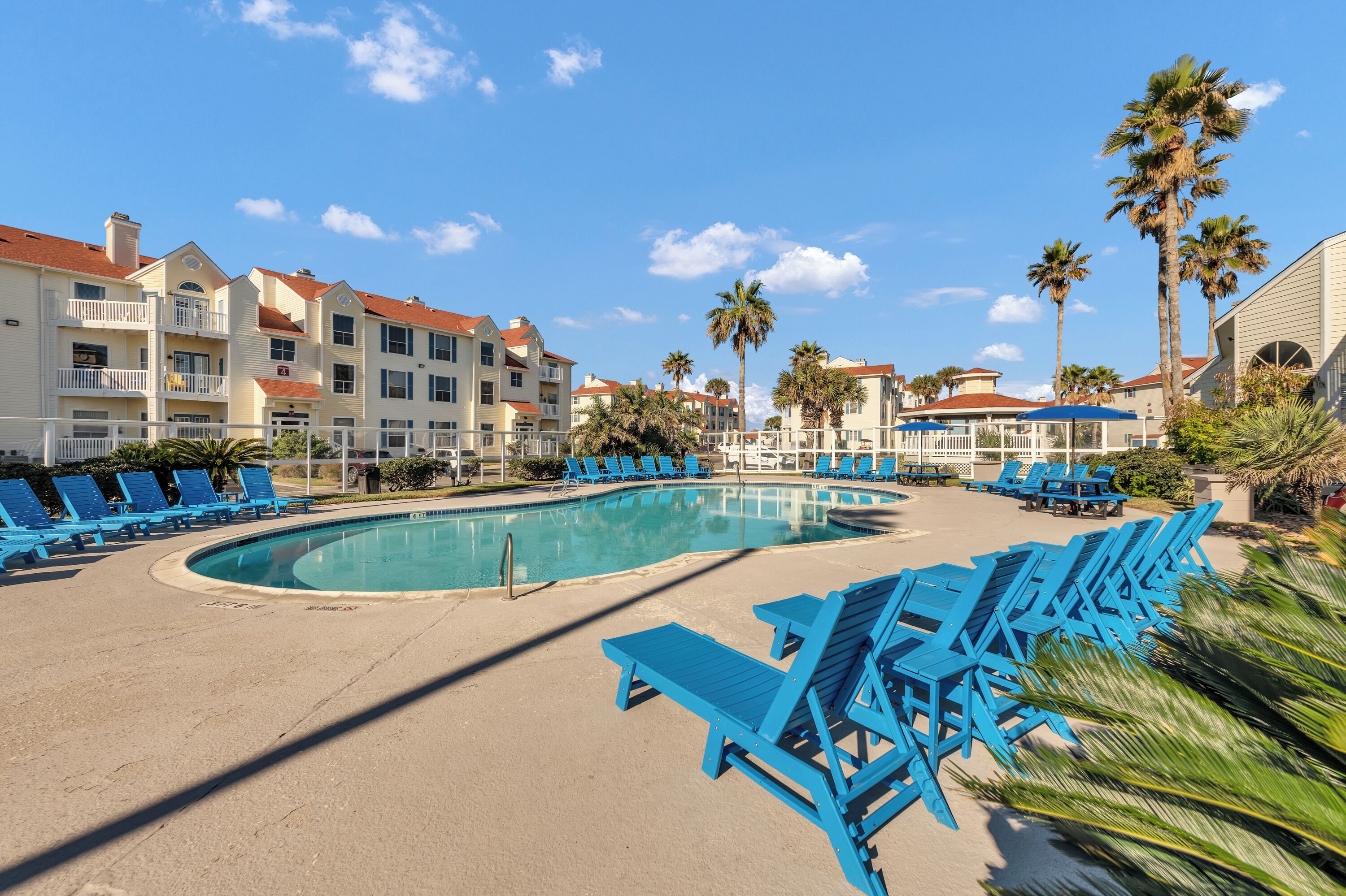 A pool area with blue lounge chairs and a clear blue sky.