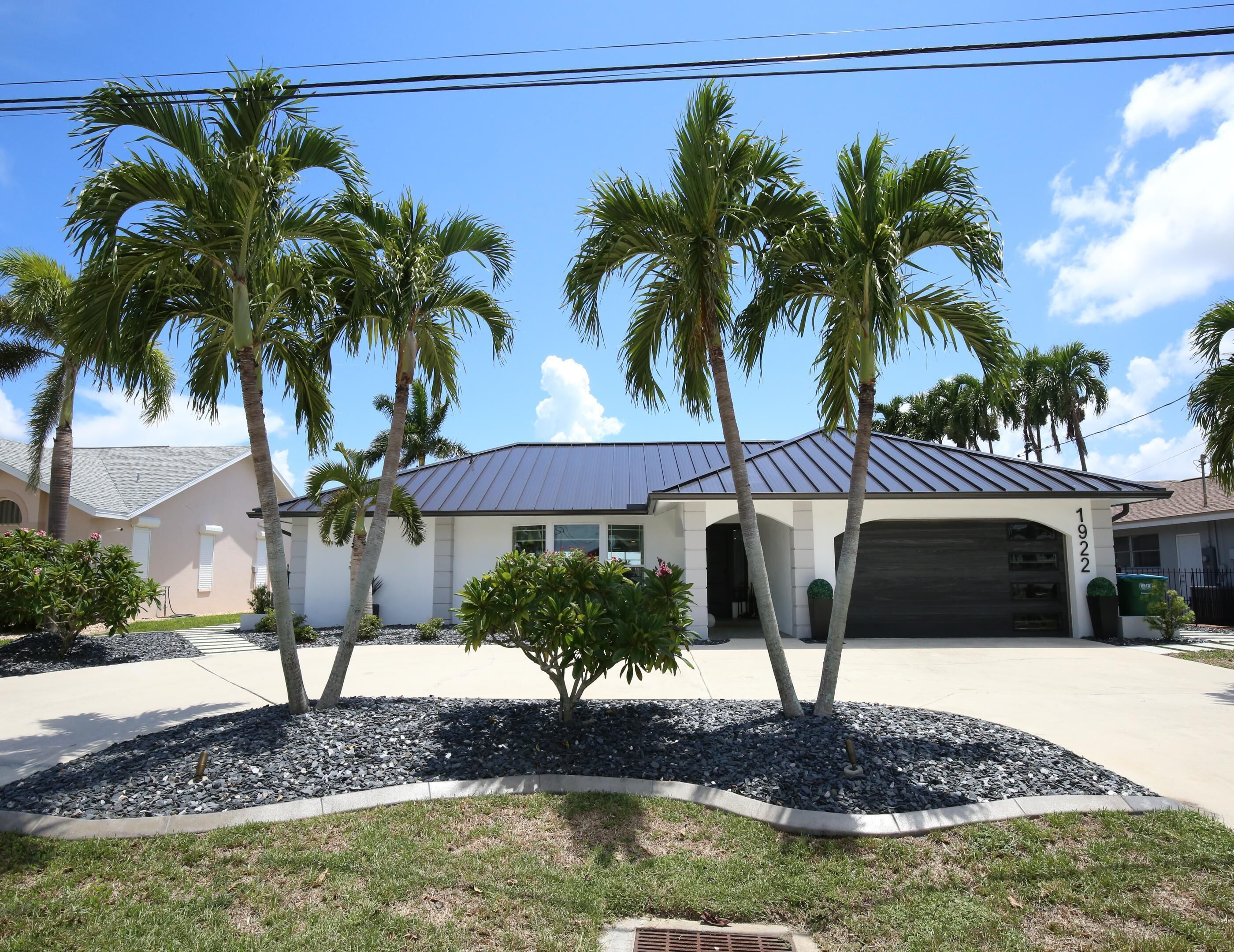A residential house with a garage, surrounded by palm trees and a well-maintained lawn.