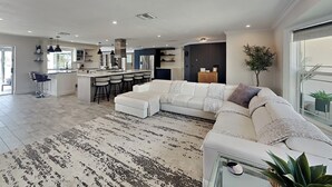 A spacious living area with a large white sofa, a kitchen with modern appliances, and a large window providing natural light. - Nauti Mermaid by Distinctive Beach Rentals (Cape Coral)