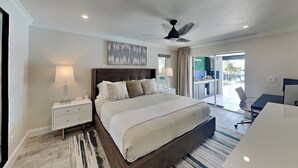 A modern bedroom with a large bed, a ceiling fan, and a view of the outdoor area. - Nauti Mermaid by Distinctive Beach Rentals (Cape Coral)