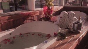 A bathtub with rose petals, a vase with flowers, and towels and champagne on a wooden bench. - Pousada Roberto Monteiro - Frente Mar (Florianópolis)