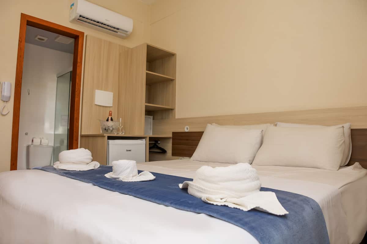 A hotel room with a bed, a wooden wardrobe, a small desk, and a mirror.