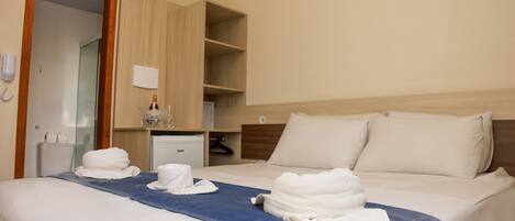 A hotel room with a bed, a wooden wardrobe, a small desk, and a mirror.