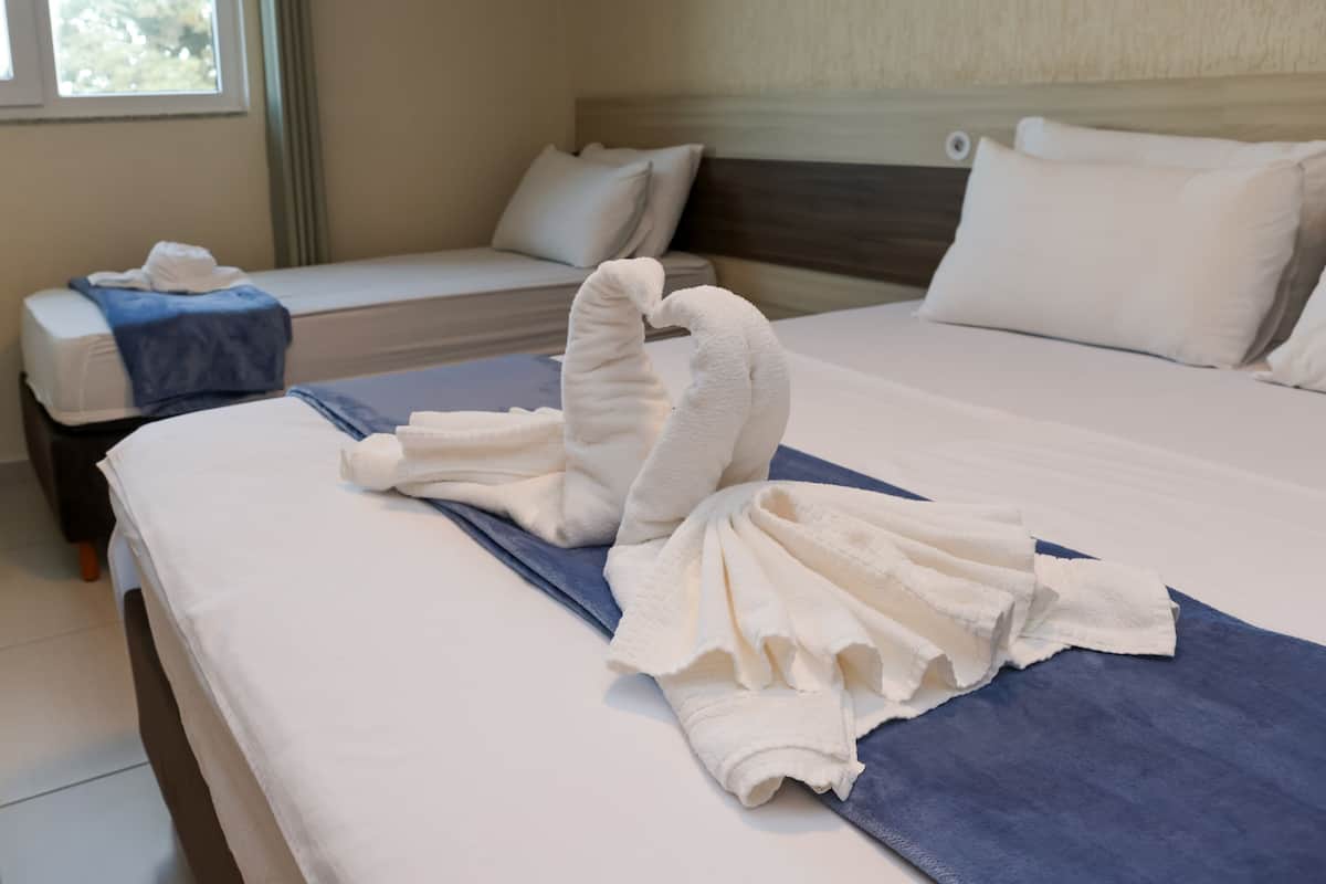 A hotel room with two beds, one with a blue towel and the other with a white towel folded into a heart shape.