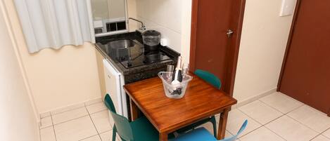 Una piccola cucina accessoriata con piano cottura, lavandino e pensili, un tavolo in legno con sedie e una porta a destra.