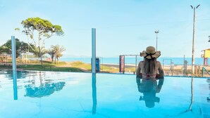 Una persona sentada junto a una piscina azul y cristalina, con vistas a la playa y palmeras.