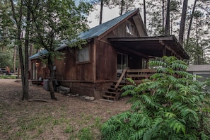 Situated in a wooded area, this cabin features a front porch with a staircase and a simple, functional design.