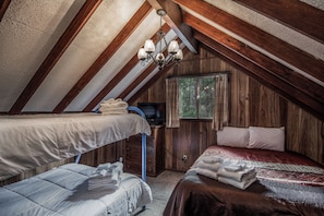 Cozy attic bedroom with two beds, a television, and a window with curtains.