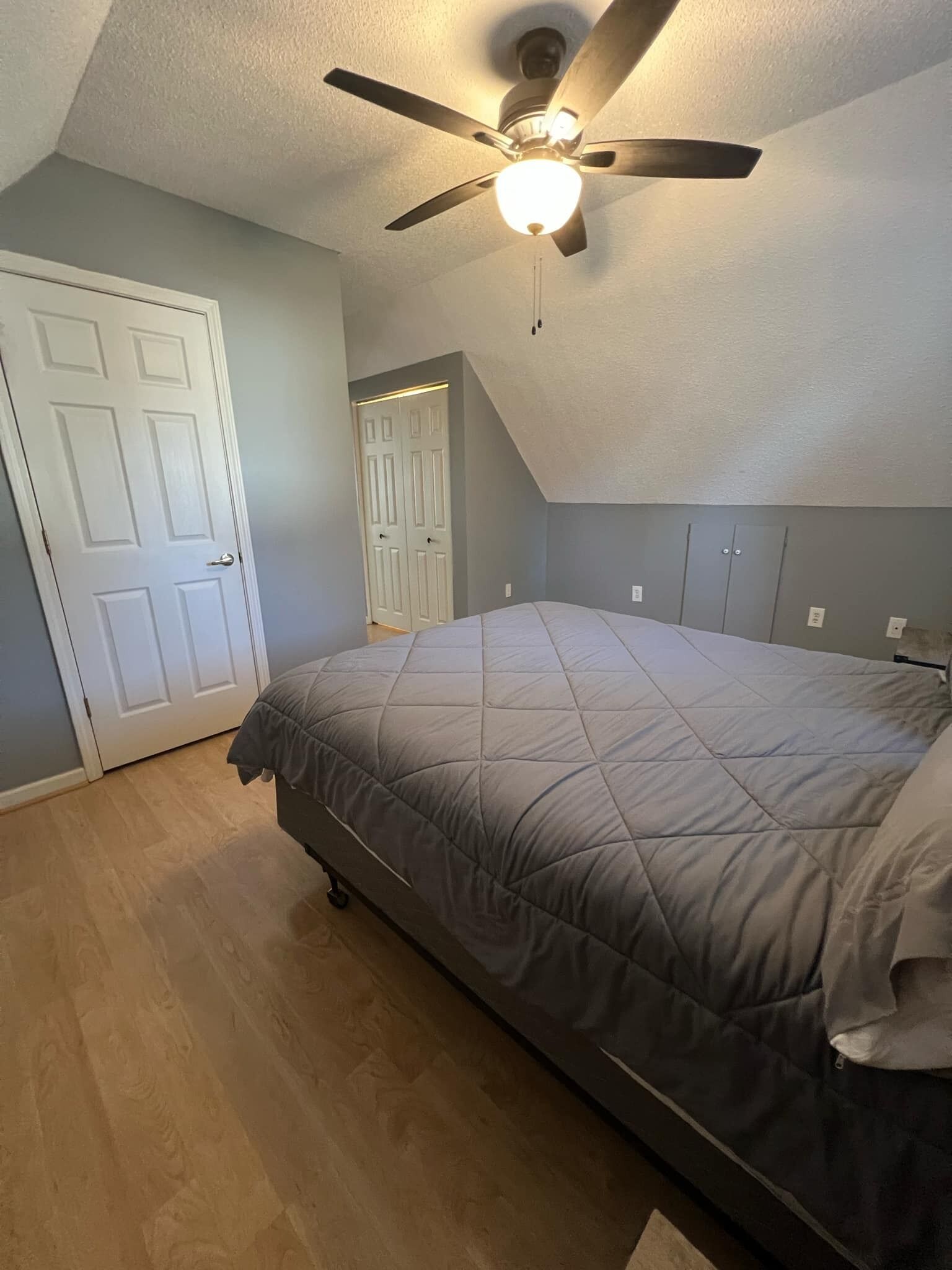 A bedroom with a bed, a ceiling fan, and a door.