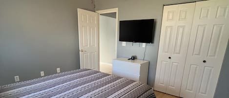 A bedroom with a bed, a ceiling fan, a TV mounted on the wall, and a wardrobe.