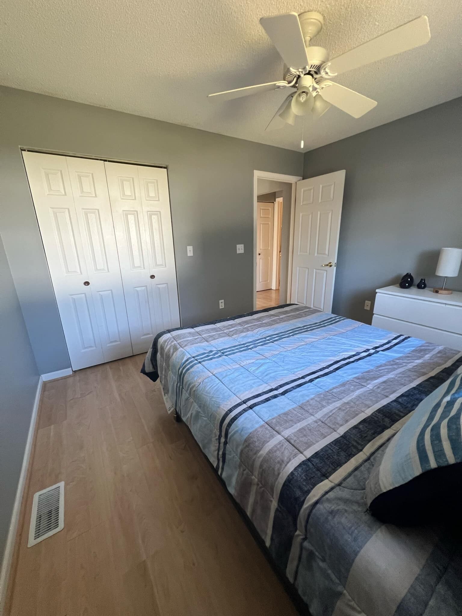 Un dormitorio con una cama, ventilador de techo, cómoda y una puerta.