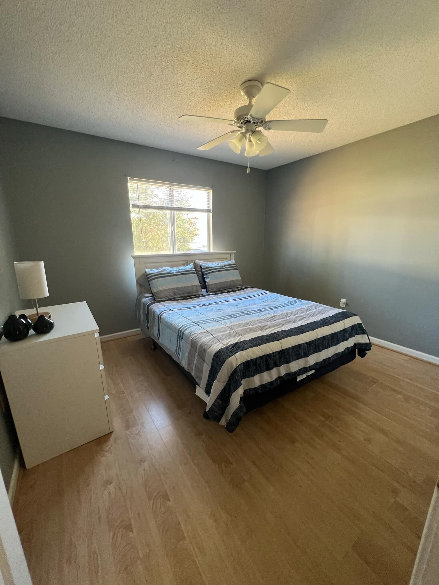 A bedroom with a bed, a nightstand, a lamp, a window, and a ceiling fan.