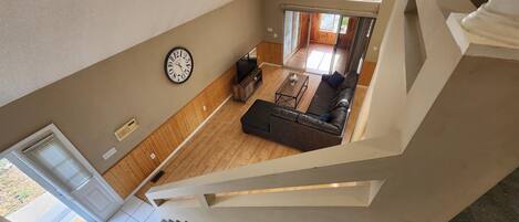 Un interior moderno con una escalera, una sala de estar con sofá y televisor, y un reloj en la pared.