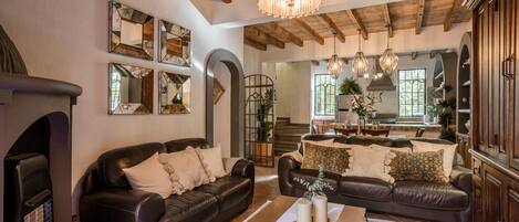 Amplia sala de estar con dos sofás de cuero, una mesa de centro y una chimenea. Hay varios espejos en las paredes, un candelabro y vistas al área de la cocina.