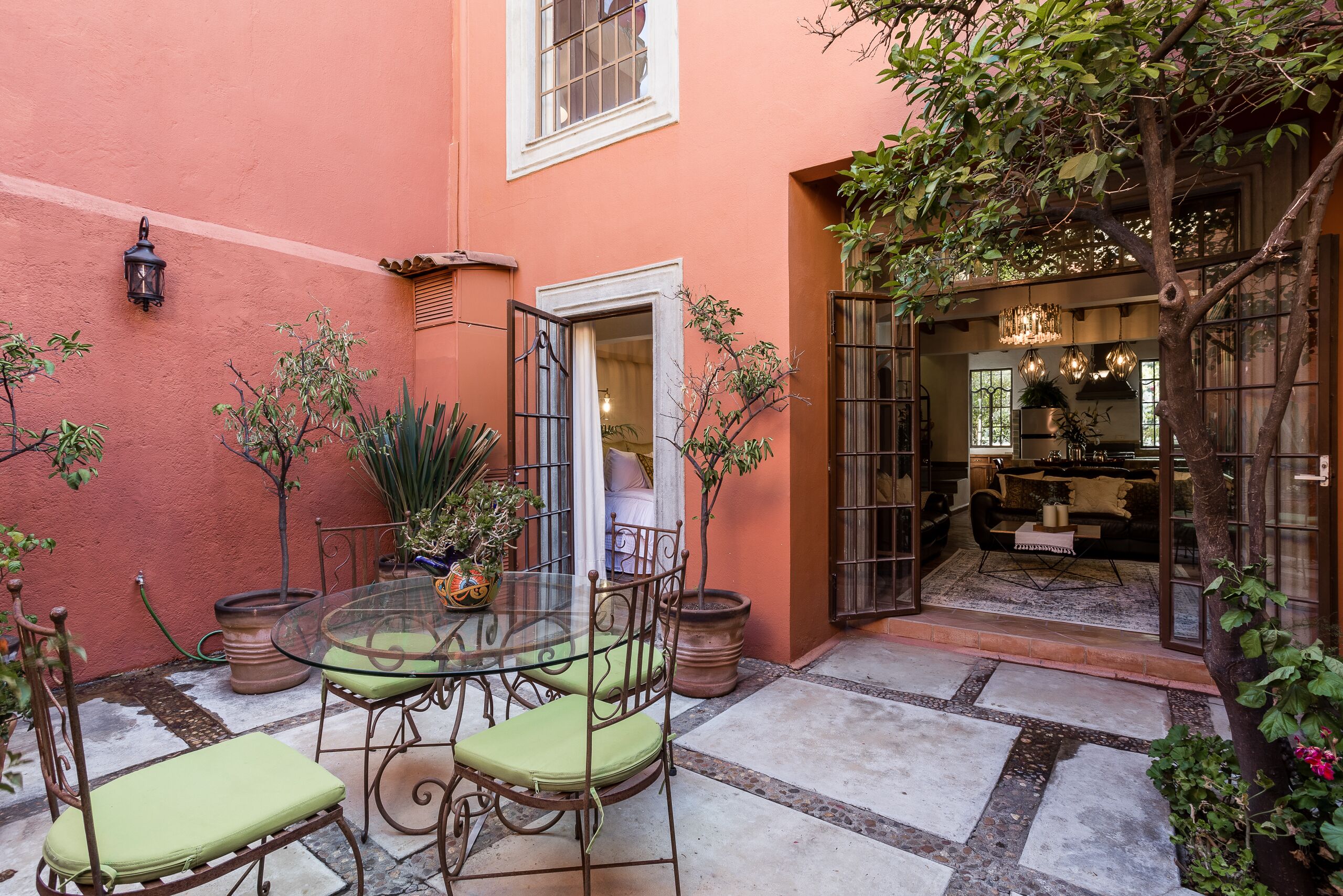 Una mesa de vidrio con sillas, una puerta y plantas en macetas en un patio.