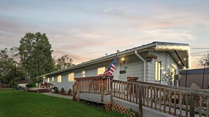 A house with a wooden deck, an American flag, and a well-maintained lawn. - Home Away from home, fully/equipped, nearJBER, private parking <4 miles Downtown (Anchorage)