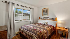 A bedroom with a bed, a nightstand, a lamp, a window with curtains, and a painting on the wall. - Home Away from home, fully/equipped, nearJBER, private parking <4 miles Downtown (Anchorage)