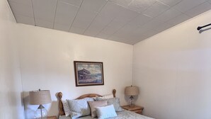 A bedroom with a large bed, two bedside tables with lamps, a nightstand with a drawer, a framed picture on the wall, and a ceiling light. - Cozy Queen with Kitchenette in Flaming Gorge (Manila)