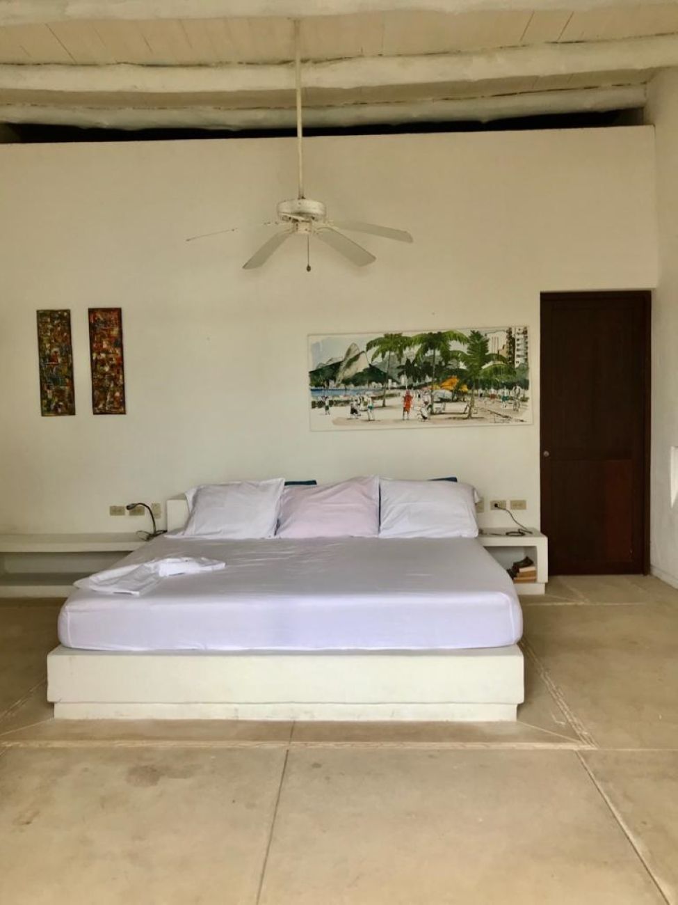 Ein Schlafzimmer mit einem Bett, einem Deckenventilator, einem Nachttisch und einem Wandbild.