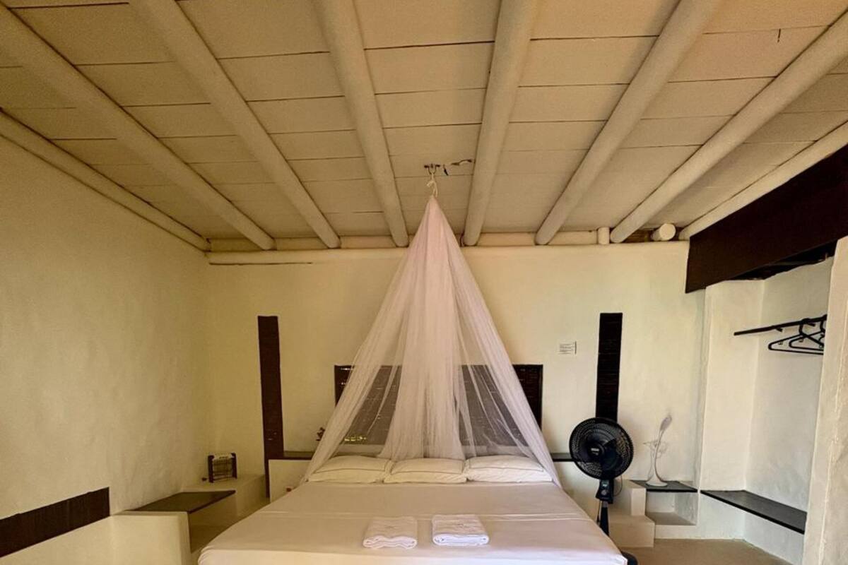 A bedroom with a canopy bed, a bedside table, and a wall-mounted fan.