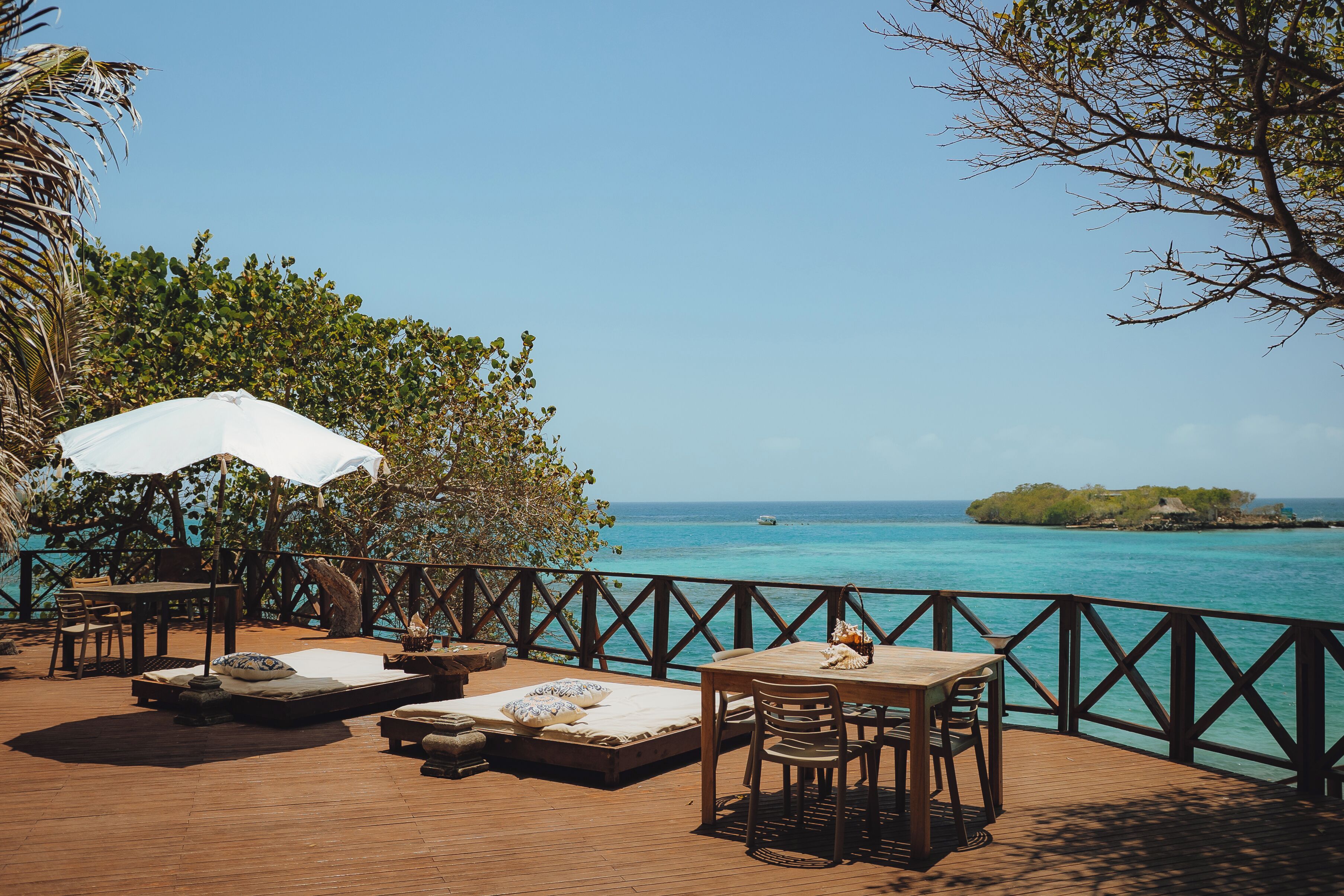 A wooden deck with lounge chairs, a table, and an umbrella overlooking a clear blue sea.