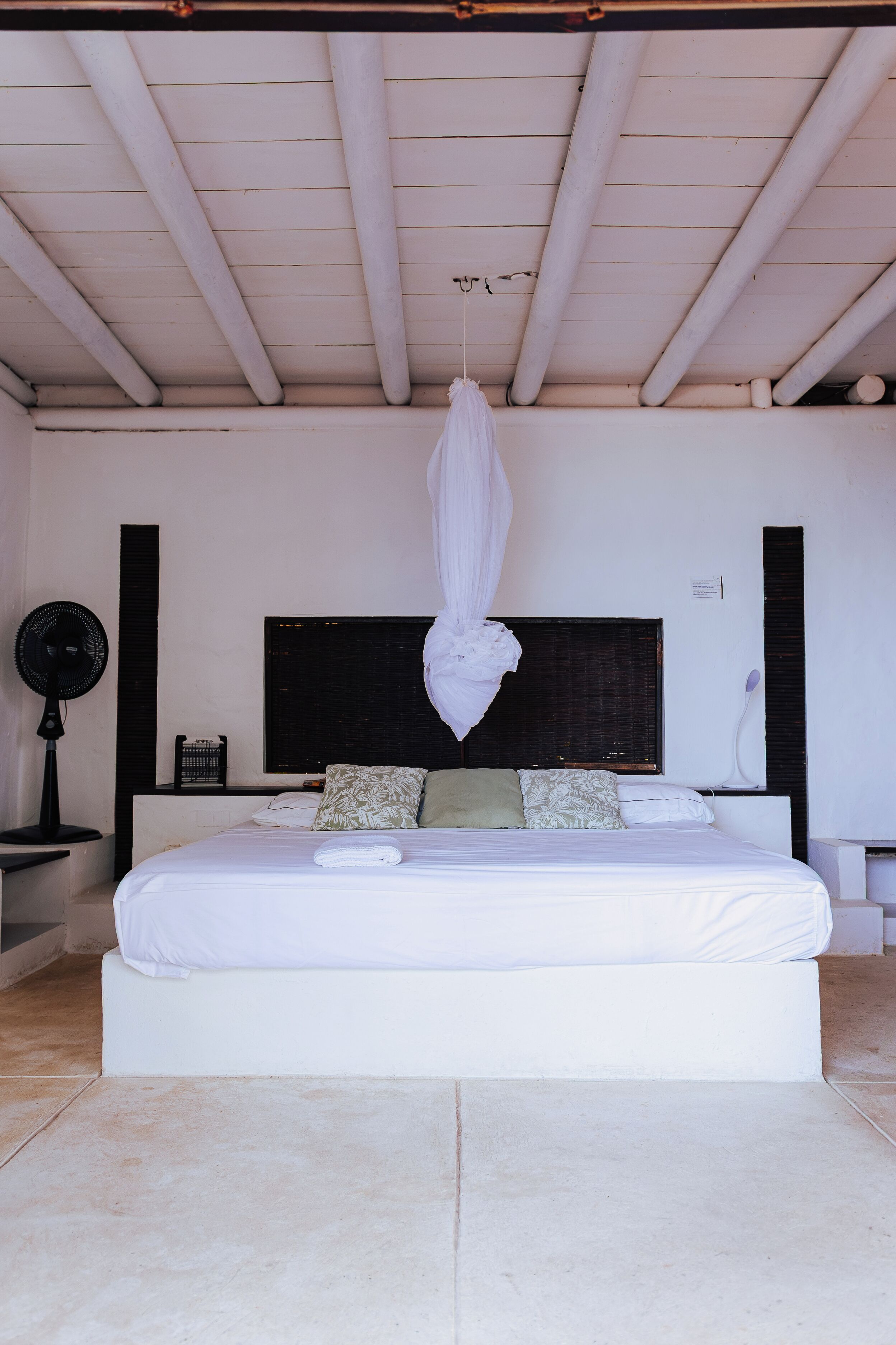 A bedroom with a large bed, a hanging canopy, a black headboard, and a bedside table with a lamp.