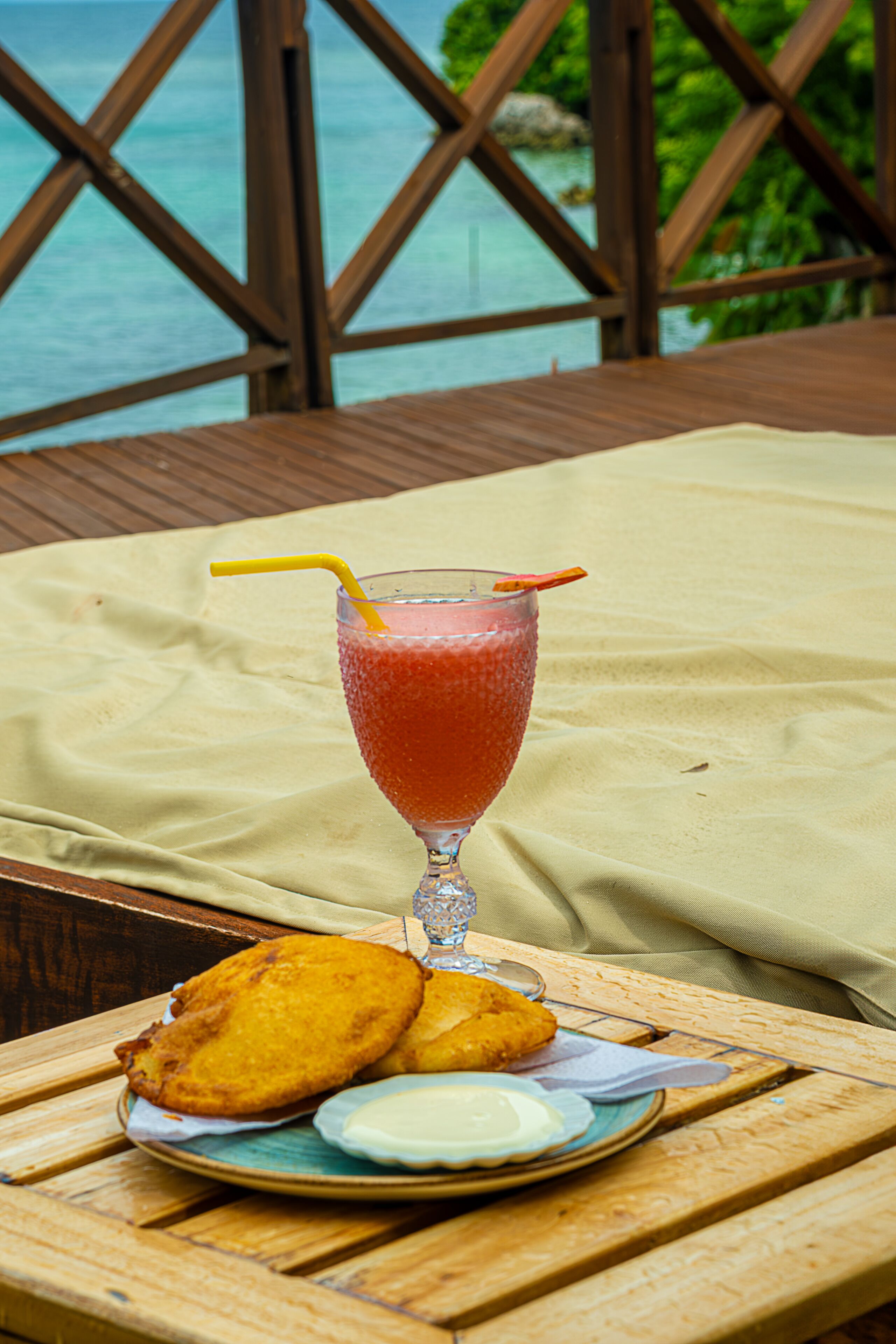 A table with a glass of drink, a plate with food, and a view of the ocean.