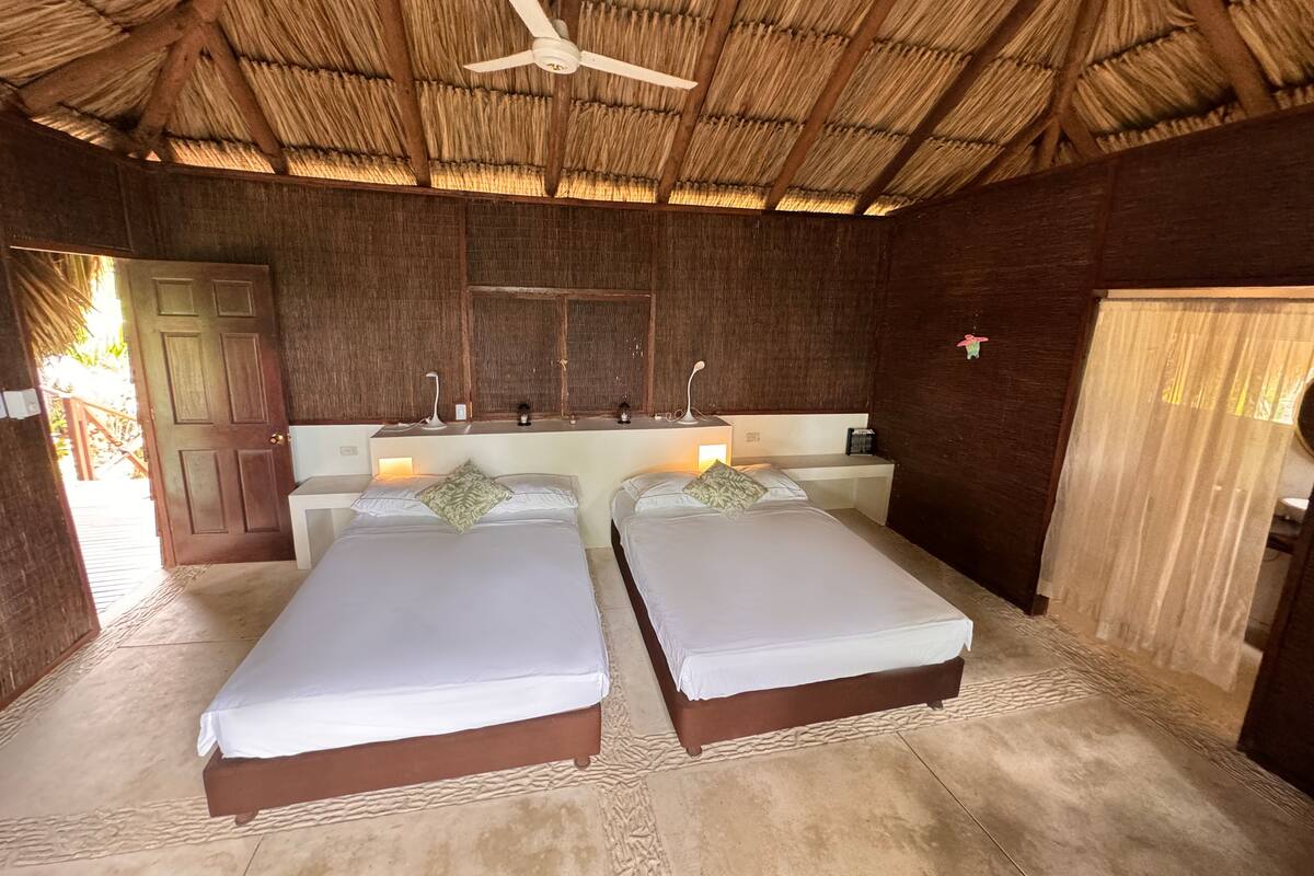 A room with two beds, a ceiling fan, a wooden ceiling, and a large window.