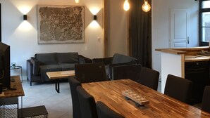 Een moderne keuken met houten kastjes en een aanrecht, een eethoek met een houten tafel en stoelen, en een zithoek met een bank en salontafel.