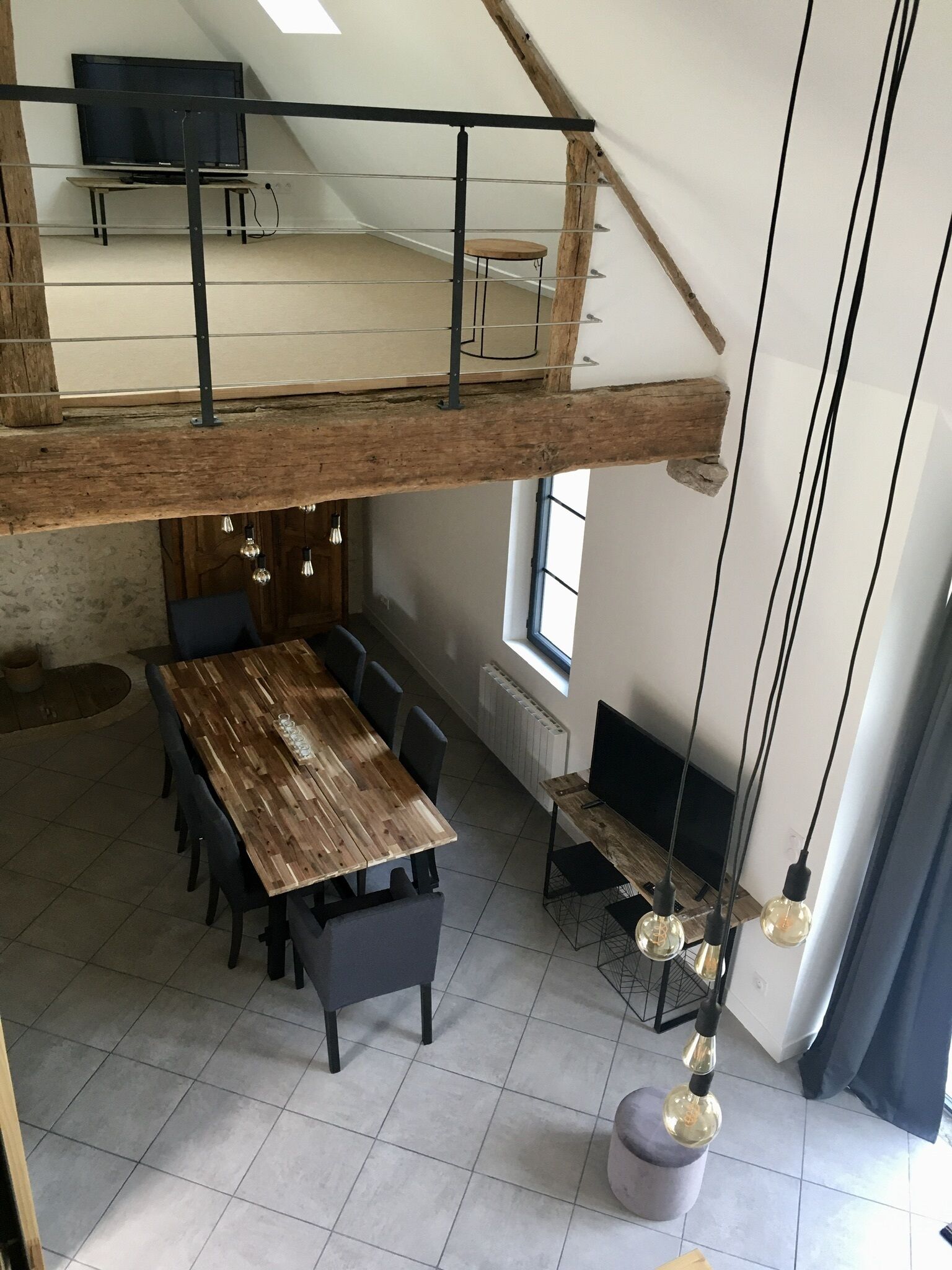 A spacious loft-style dining area with a high ceiling, exposed wooden beams, and a long wooden table surrounded by chairs.