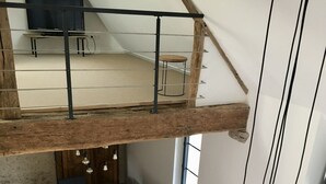 Een ruime eetruimte in loftstijl met een hoge plafond, zichtbare houten balken en een lange houten tafel omringd door stoelen.