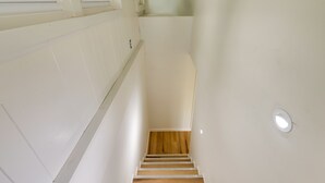 Una escalera de madera con paredes blancas que conduce a una plataforma con ventanal.